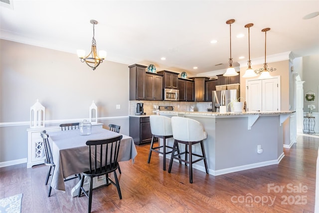 kitchen featuring a kitchen breakfast bar, hanging light fixtures, tasteful backsplash, dark brown cabinetry, and stainless steel appliances