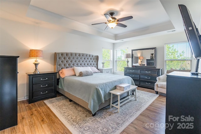 bedroom with light wood-type flooring, a tray ceiling, ceiling fan, and crown molding