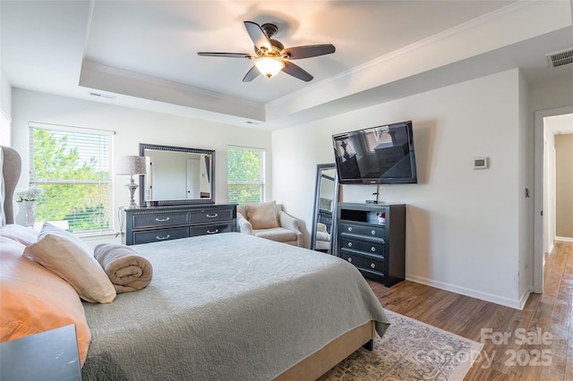 bedroom with hardwood / wood-style flooring, ceiling fan, a raised ceiling, and multiple windows