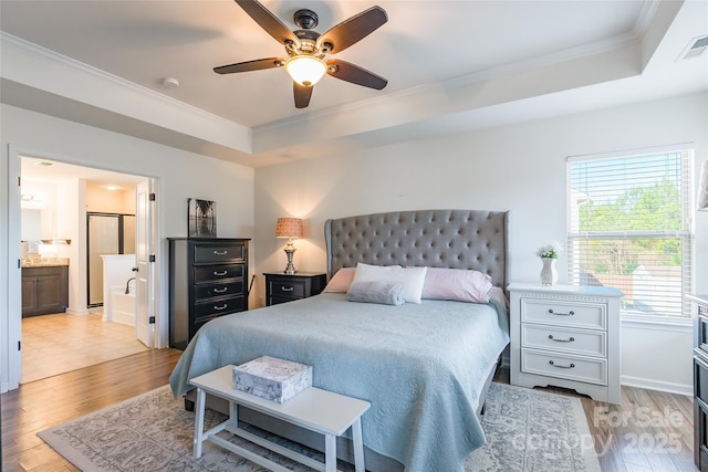 bedroom featuring ensuite bathroom, a raised ceiling, light hardwood / wood-style flooring, ceiling fan, and ornamental molding