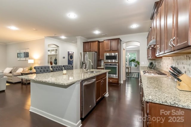 kitchen featuring backsplash, a center island with sink, a kitchen breakfast bar, appliances with stainless steel finishes, and light stone counters