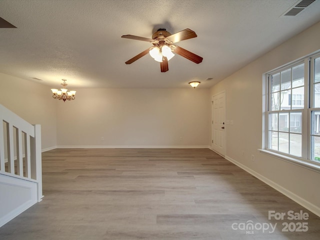 empty room featuring ceiling fan with notable chandelier, light hardwood / wood-style flooring, and plenty of natural light