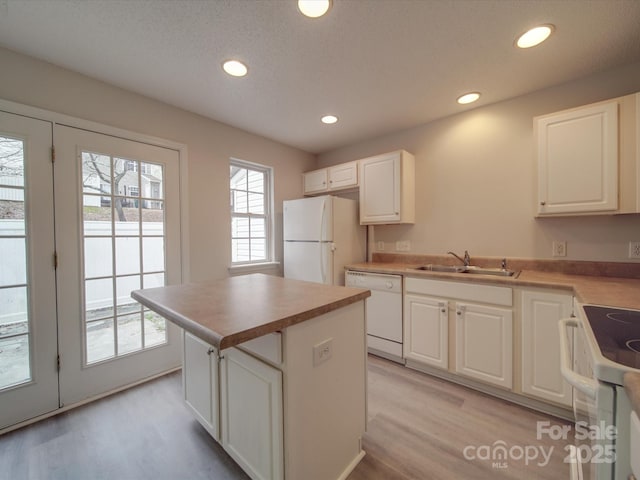 kitchen featuring white appliances, sink, a center island, light hardwood / wood-style floors, and white cabinetry