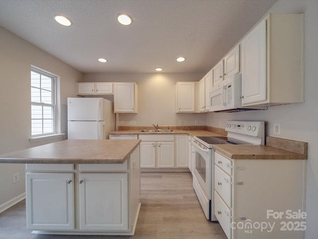 kitchen featuring white cabinets, a kitchen island, white appliances, and sink