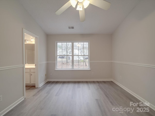 unfurnished bedroom featuring ensuite bath, ceiling fan, lofted ceiling, a textured ceiling, and light wood-type flooring