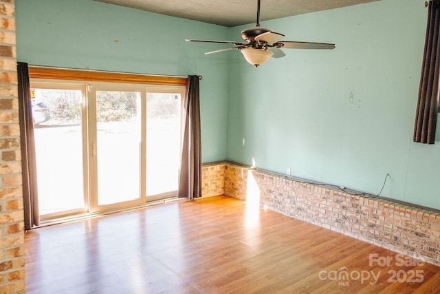 spare room with light hardwood / wood-style floors, ceiling fan, and brick wall