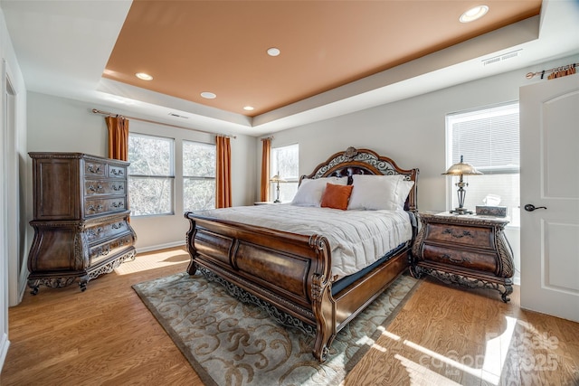 bedroom with hardwood / wood-style floors and a tray ceiling