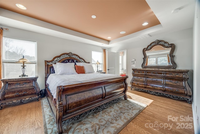 bedroom with light hardwood / wood-style floors and a raised ceiling