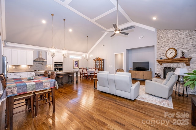 living room featuring ceiling fan with notable chandelier, hardwood / wood-style flooring, high vaulted ceiling, and a stone fireplace