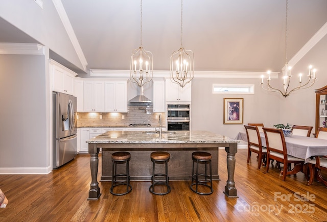 kitchen with decorative light fixtures, white cabinetry, stainless steel appliances, and an island with sink