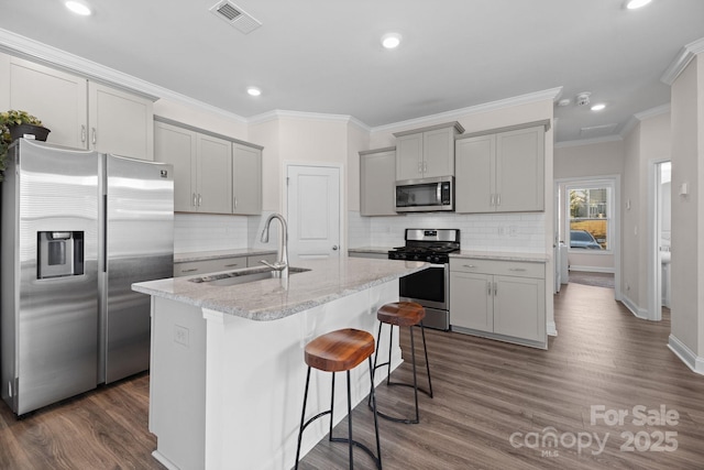 kitchen featuring visible vents, a kitchen island with sink, a sink, gray cabinetry, and stainless steel appliances