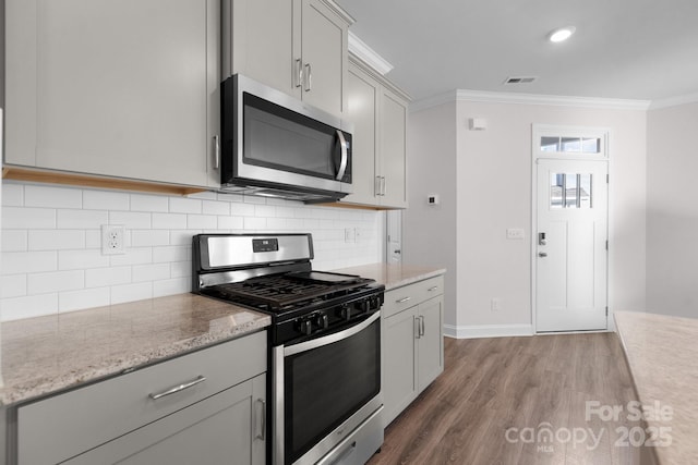 kitchen featuring visible vents, stainless steel appliances, wood finished floors, and ornamental molding