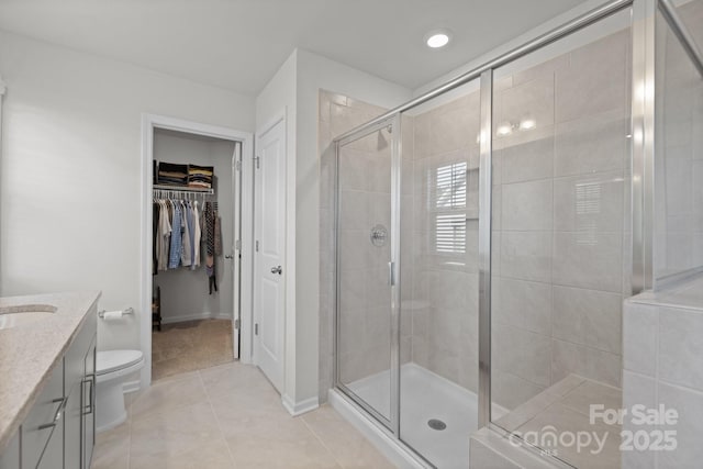 bathroom with vanity, a shower stall, a walk in closet, tile patterned floors, and toilet