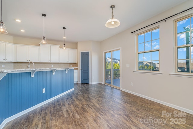 kitchen with white cabinets, a kitchen breakfast bar, light stone counters, and pendant lighting