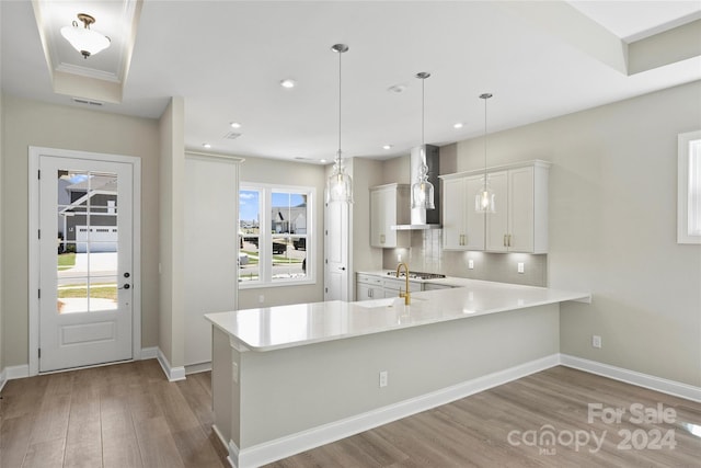 kitchen featuring kitchen peninsula, backsplash, wall chimney exhaust hood, pendant lighting, and white cabinets