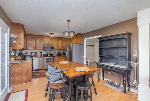 kitchen featuring light wood-type flooring, decorative backsplash, stainless steel appliances, and pendant lighting