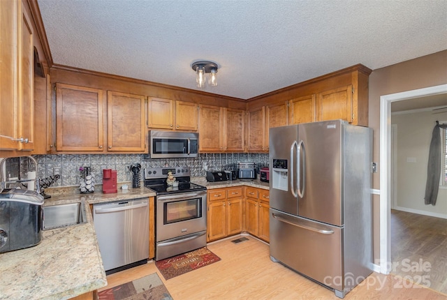 kitchen with light wood-type flooring, appliances with stainless steel finishes, decorative backsplash, and light stone counters