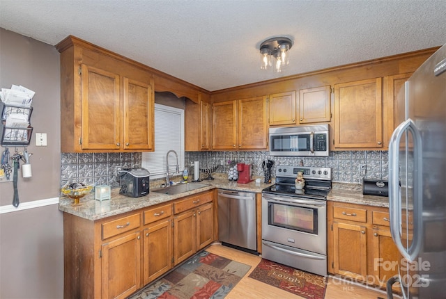 kitchen featuring stainless steel appliances, decorative backsplash, light stone countertops, a textured ceiling, and sink