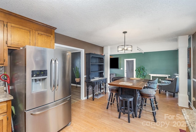 kitchen with decorative light fixtures, light hardwood / wood-style floors, a breakfast bar, a textured ceiling, and stainless steel fridge