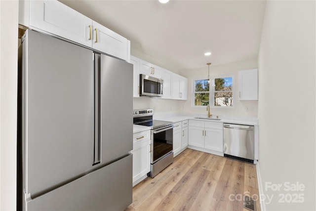 kitchen featuring light wood-type flooring, stainless steel appliances, sink, white cabinets, and hanging light fixtures