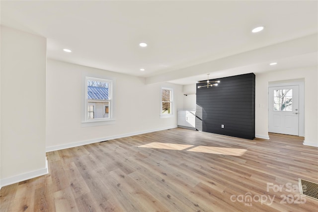 unfurnished living room featuring a healthy amount of sunlight, light wood-type flooring, and a chandelier