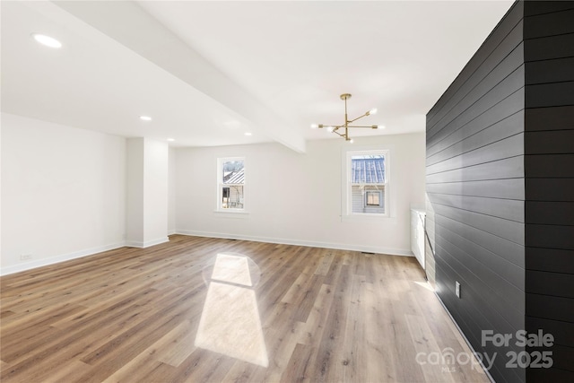 unfurnished living room with beam ceiling, light hardwood / wood-style floors, a healthy amount of sunlight, and an inviting chandelier