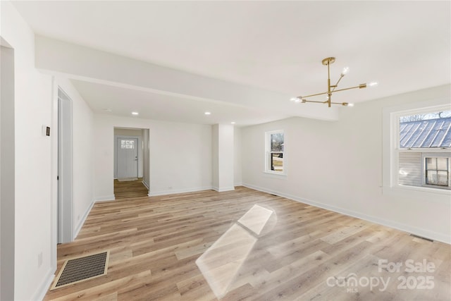 spare room with a wealth of natural light, light hardwood / wood-style floors, and an inviting chandelier