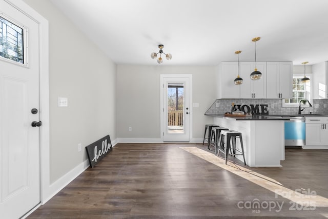 kitchen featuring white cabinetry, hanging light fixtures, stainless steel dishwasher, plenty of natural light, and a breakfast bar area