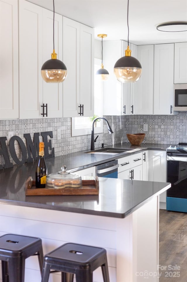 kitchen featuring a kitchen bar, white cabinets, pendant lighting, and appliances with stainless steel finishes