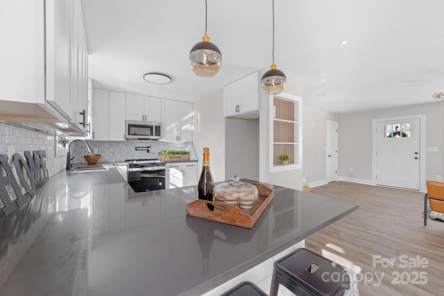 kitchen with backsplash, white cabinets, decorative light fixtures, kitchen peninsula, and stainless steel appliances