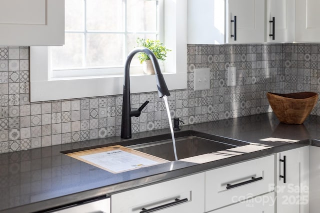 kitchen with backsplash, white cabinetry, and sink