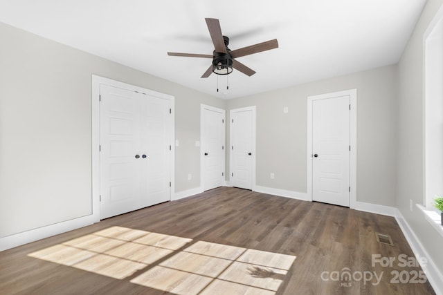 unfurnished bedroom with multiple closets, ceiling fan, and hardwood / wood-style flooring