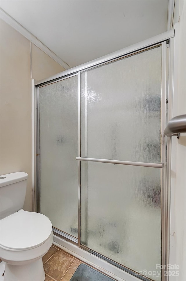 bathroom featuring toilet, a shower with door, and crown molding