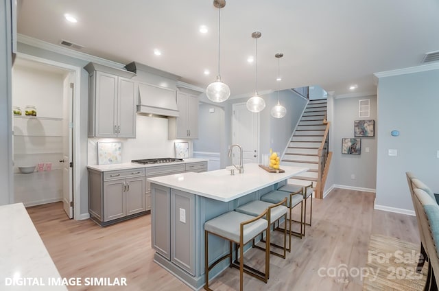 kitchen featuring a kitchen bar, stainless steel gas cooktop, sink, gray cabinets, and hanging light fixtures