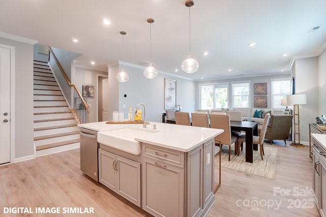 kitchen featuring sink, light hardwood / wood-style flooring, stainless steel dishwasher, decorative light fixtures, and a center island with sink