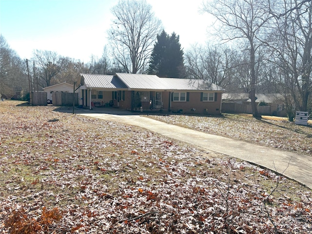 ranch-style house with metal roof, concrete driveway, and fence