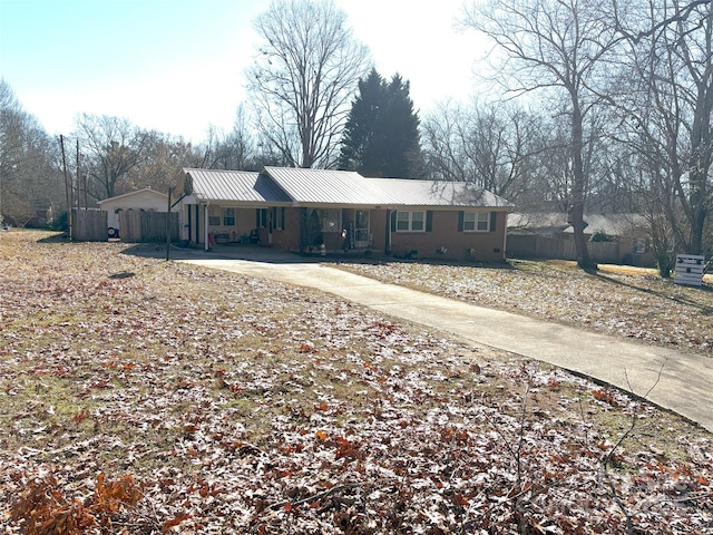 ranch-style house with metal roof, concrete driveway, and fence