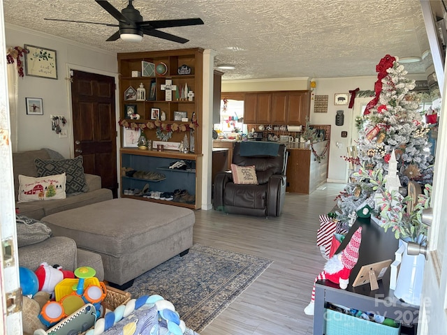 living room with ceiling fan, light hardwood / wood-style floors, a textured ceiling, and ornamental molding