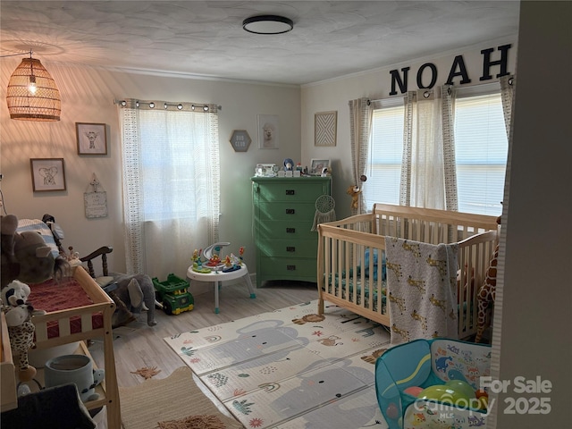 bedroom with crown molding, a crib, and hardwood / wood-style flooring