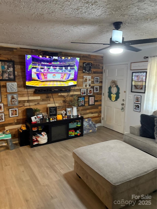 living area featuring a textured ceiling, wood finished floors, a ceiling fan, and wooden walls