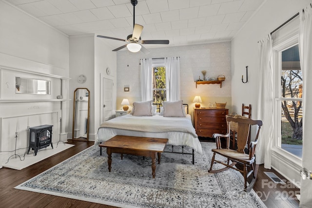 bedroom featuring ceiling fan, dark hardwood / wood-style floors, and a wood stove