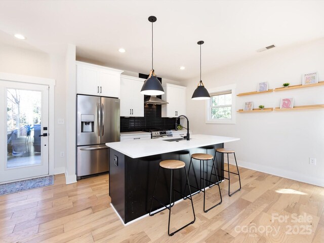 kitchen featuring white cabinetry, an island with sink, decorative backsplash, a breakfast bar, and appliances with stainless steel finishes