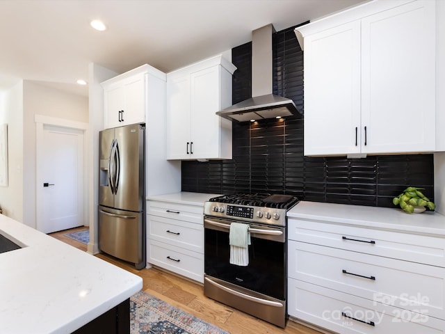 kitchen with white cabinets, wall chimney range hood, appliances with stainless steel finishes, tasteful backsplash, and light hardwood / wood-style floors