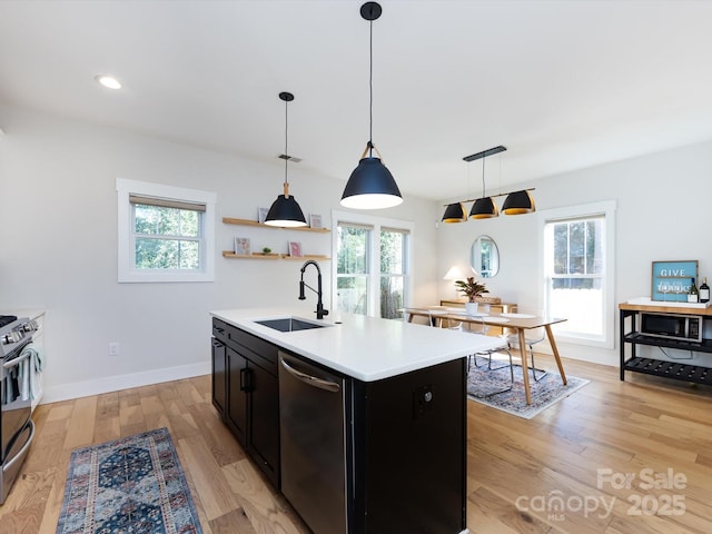 kitchen with sink, light hardwood / wood-style flooring, an island with sink, decorative light fixtures, and appliances with stainless steel finishes