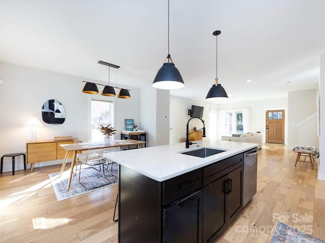 kitchen featuring pendant lighting, dishwasher, a kitchen island with sink, sink, and light wood-type flooring