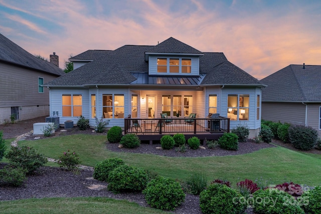 back house at dusk with a deck and a lawn