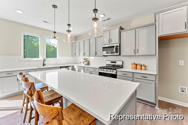 kitchen with a center island, wood-type flooring, decorative light fixtures, and appliances with stainless steel finishes