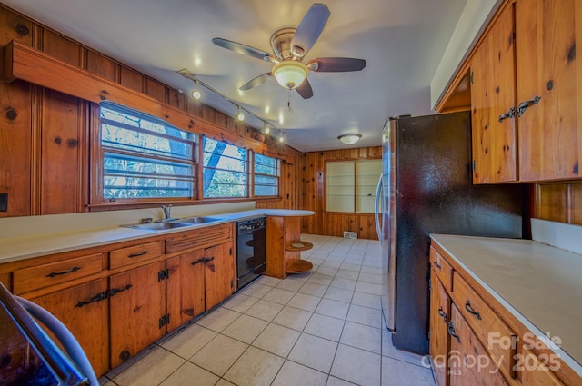 kitchen with ceiling fan, dishwasher, sink, wood walls, and light tile patterned flooring