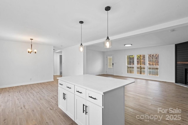 kitchen featuring a large fireplace, beamed ceiling, white cabinets, a center island, and hanging light fixtures