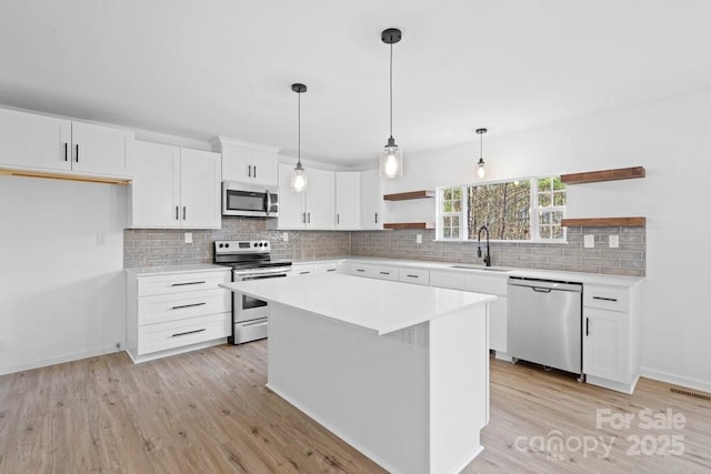 kitchen featuring white cabinetry, sink, decorative light fixtures, a kitchen island, and appliances with stainless steel finishes